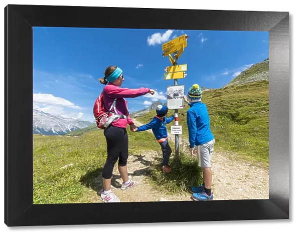 Mother and sons look at the signpost of hiking trails, Spluga Pass, Chiavenna Valley