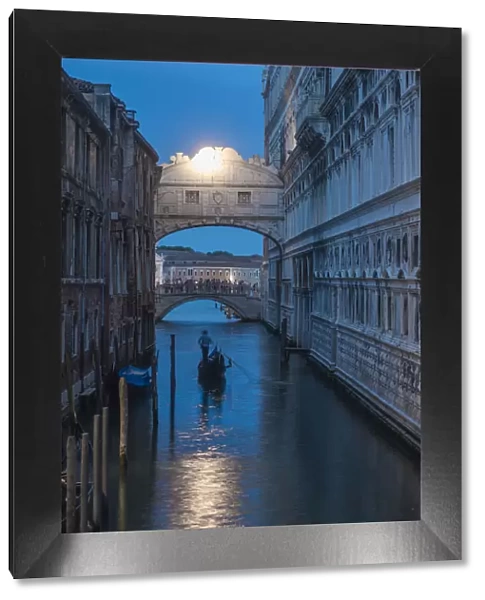 Gondolas pass under the Bridge of Sighs beside the Doges Palace in Venice at twilight