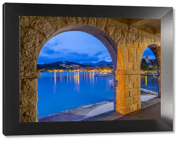 View of town and Crkva Sv. Nikole church through arches at dusk, Cavtat on the Adriatic