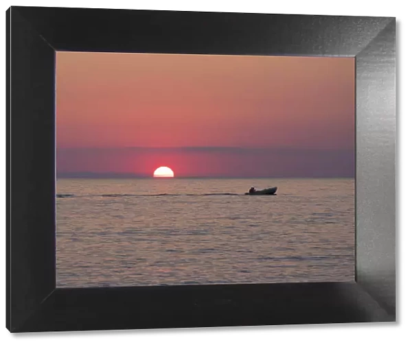 View across the Tyrrhenian Sea at sunrise, small boat crossing Calura Bay, Cefalu