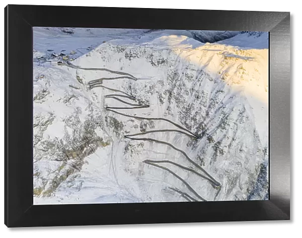 Narrow bends of the Stelvio Pass road on steep snowy mountain ridge, aerial view by drone