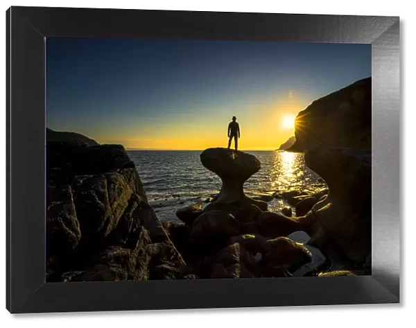 Silhouette of man admiring sunset standing on top of Kannesteinen rock, Oppedal, Vagsoy