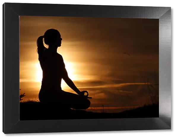 Silhouette of a woman in lotus position, practising yoga against the light of the evening