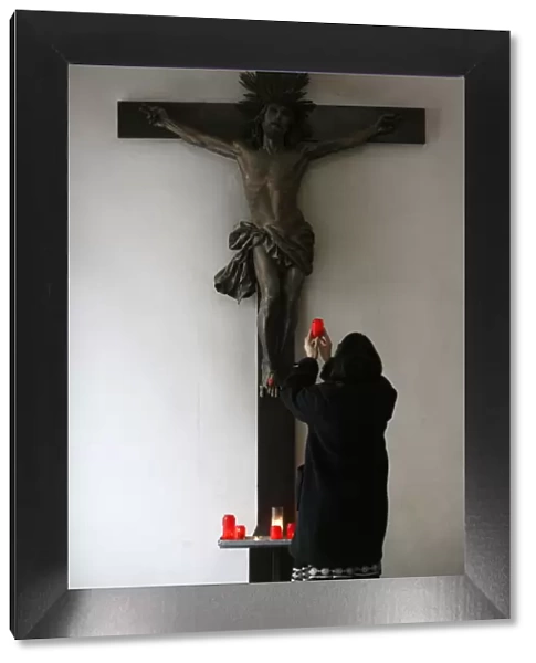 Woman offering candle and praying in front of Crucifix