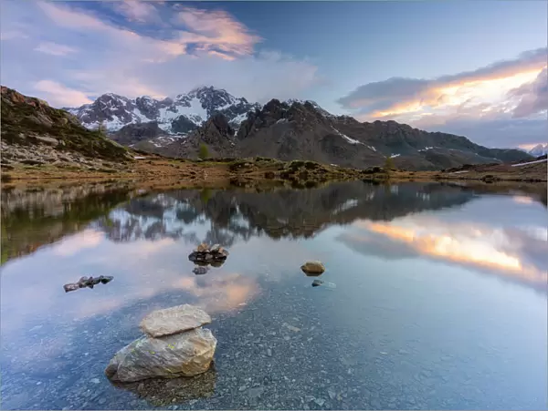 Sunrise lit the rocky peak of Monte Disgrazia mirrored in the clear water of lake Zana