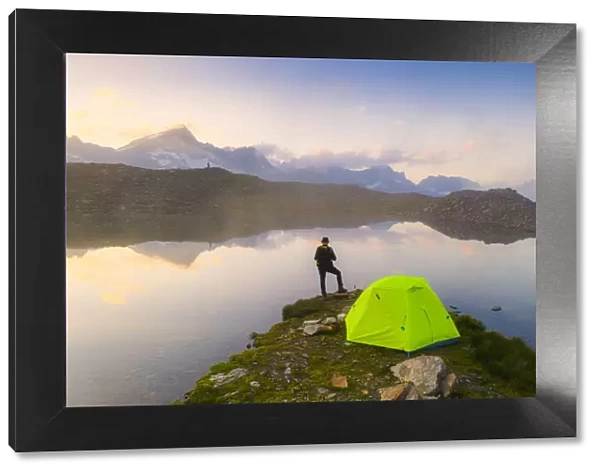Rear view of man with hat standing outside tent at Obere Schwarziseeli lake at dawn
