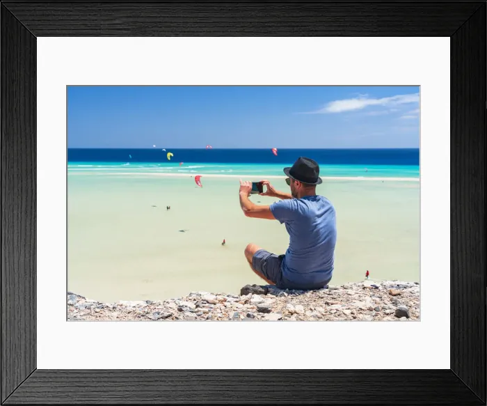 Framed Print : Tourist with straw hat photographing kiteboarders with smartphone at Sotavento beach