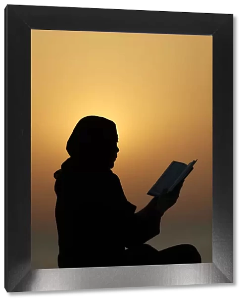Silhouette of a Muslim woman reading the Noble Quran at sunset, United Arab Emirates