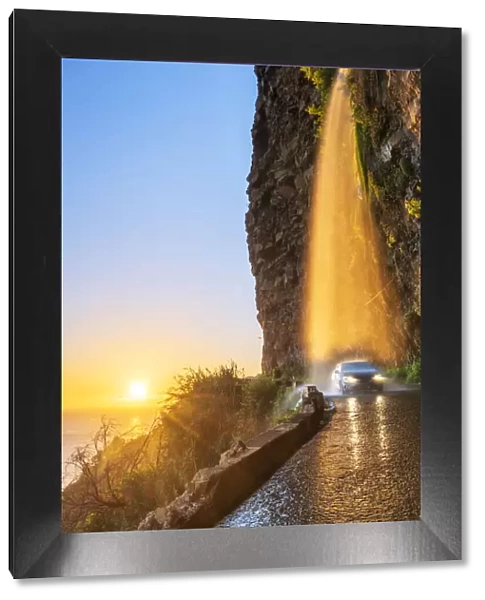 Car passing under Anjos waterfall on slippery coastal road at sunset, Ponta do Sol