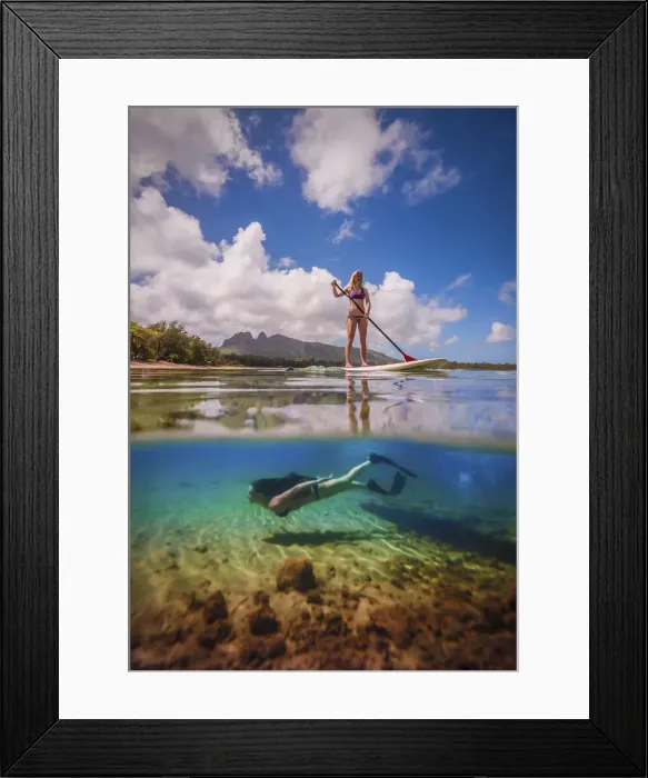 Framed Print : An athletic woman rides a stand-up paddle-board as another woman free-dives below her Framed Print : An athletic woman rides a stand-up paddle-board as another woman free-dives below her