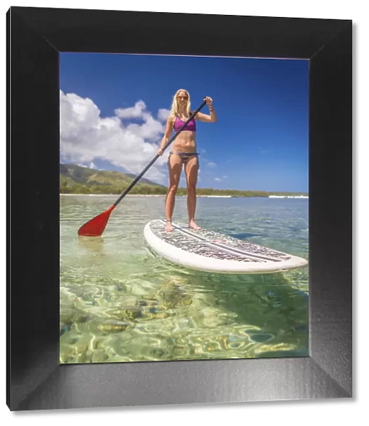 A young athletic woman using a stand-up paddle-board in a calm bay of Hawaii
