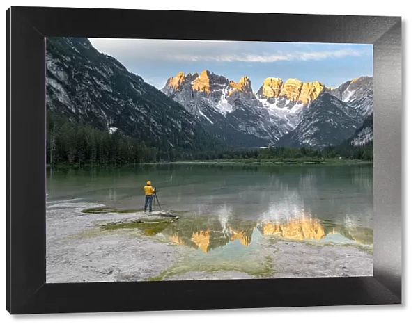 Photographer with tripod admiring the Dolomites at dawn from lake Landro, Dolomites