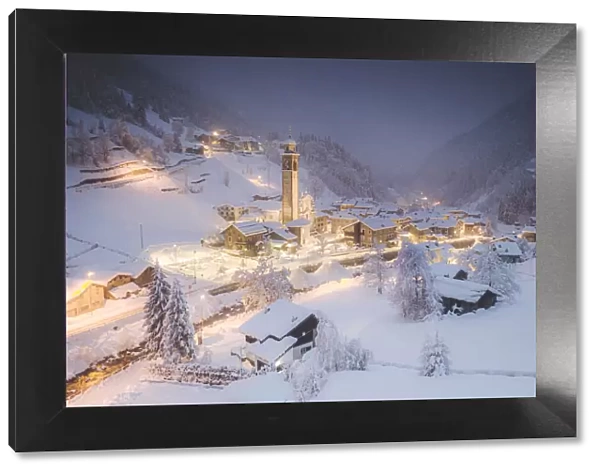 Illuminated village of Gerola Alta and frozen river covered with snow during winter dusk