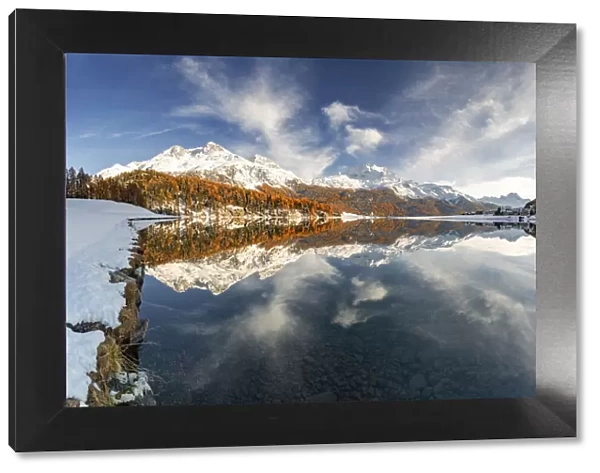 Autumn woods and snowcapped mountains mirrored in the clear water of Champfer lake at
