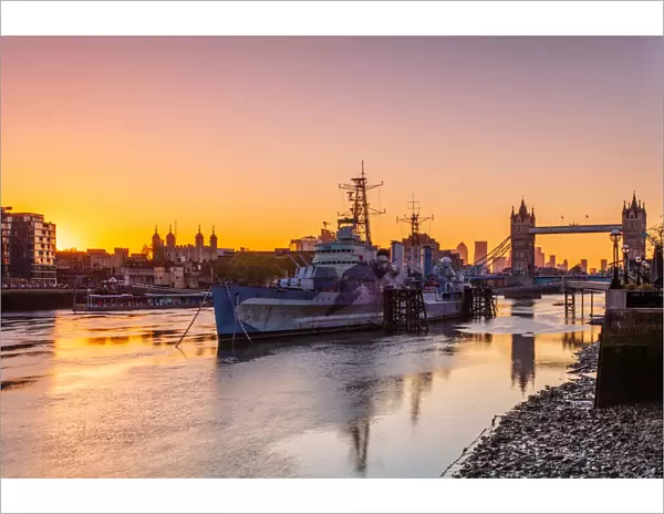 HMS Belfast and Tower Bridge at sunrise with a low tide on the River Thames, London