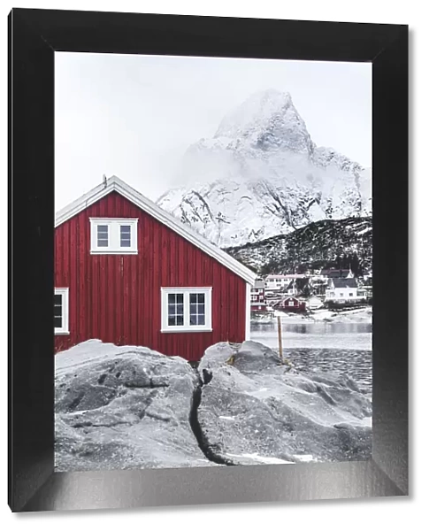 Red Rorbu in the frozen landscape with snowcapped Olstind mountain in the background, Reine, Nordland, Lofoten Islands, Norway, Scandinavia, Europe