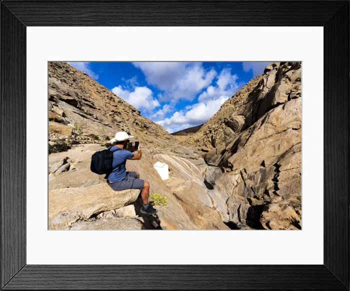 Framed Print : Tourist photographing canyons with smartphone sitting on rocks at Barranco de las Penitas, Fuerteventura, Canary Islands, Spain, Atlantic, Europe Framed Print : Tourist photographing canyons with smartphone sitting on rocks at Barranco de las Penitas, Fuerteventura, Canary Islands, Spain, Atlantic, Europe