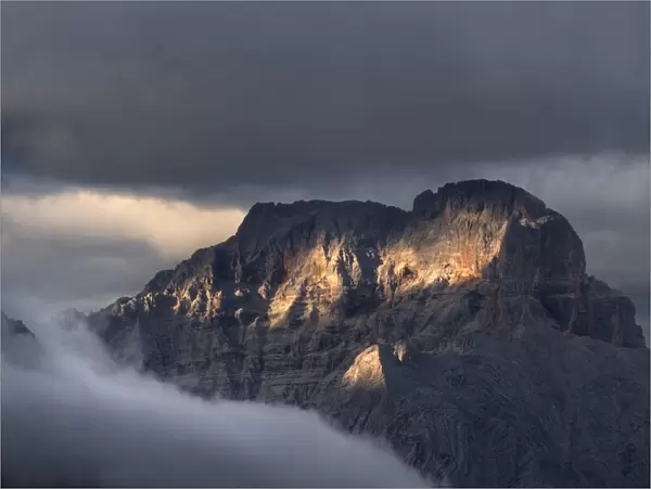 Sunset on Croda Rossa d Ampezzo mountains surrounded by the fog and darkness with only a few spots of sun light, Dolomites, Veneto, Italy, Europe