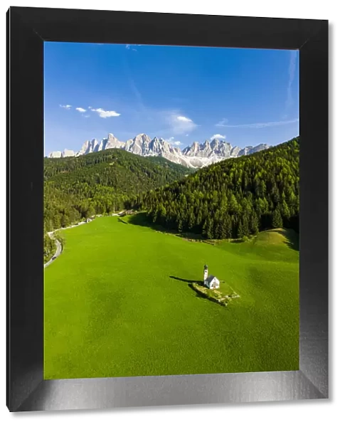 Green forest and meadows surrounding the small Ranui church and Odle in spring, aerial view, Funes Valley, Dolomites, South Tyrol, Italy, Europe