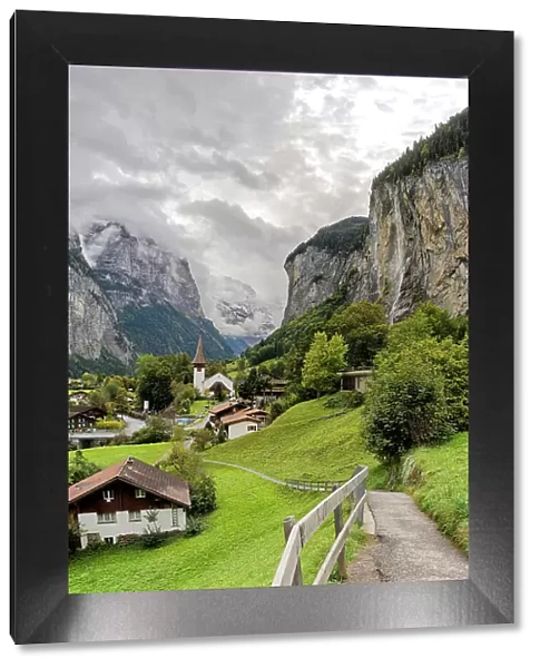 Path among green meadows of the alpine village of Lauterbrunnen with Trummelbach Falls in the background, Bern canton, Switzerland, Europe