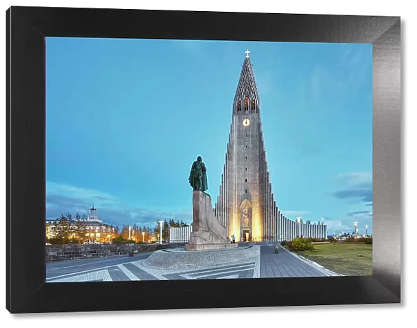 A dusk view of the spire of Hallgrimskirkja Church, fronted by a statue of Leifur Eriksson, founder of Iceland, in central Reykjavik, Iceland, Polar Regions