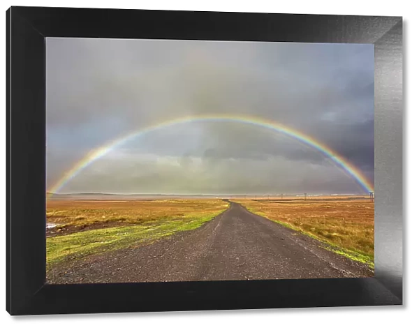 A rainbow straddles a road in countryside near Rif, Snaefellsnes peninsula, western Iceland, Polar Regions