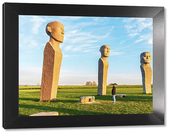 Tourist admiring Dodekalitten statues at sunset, Lolland island, Zealand region, Denmark, Europe