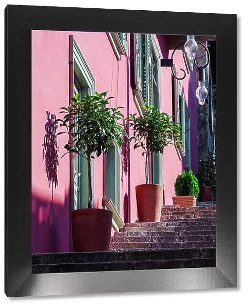 A staircase with large decorative plant pots outside a traditional house with a vivid wall color and wooden shutters in Nafplion, Peloponnese, Greece, Europe