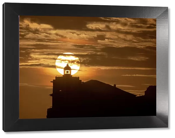 Sun aligned with the silhouette of the lighthouse of Luarca, Asturias, Spain, Europe