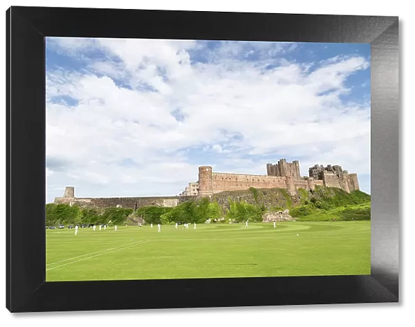 Bamburgh Castle, a medieval fortress, Grade I Listed Building constructed on top of a craggy outcrop of volcanic dolerite, overlooking a cricket ground, Bamburgh, Northumberland, England, United Kingdom, Europe