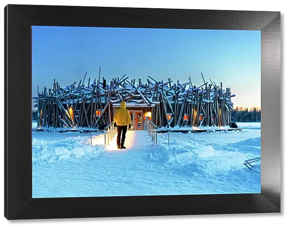 Person stands on the bridge connecting the main building of the illuminated Arctic Bath hotel made of logs, dusk time, Harads, Swedish Lapland, Norrbotten, Sweden, Scandinavia, Europe
