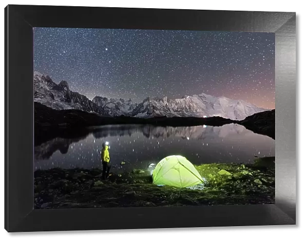 Person admiring the starry sky outside tent pitched on the shore of Cheserys lake surrounded by alpine landscape of Mont Blanc, Chamonix, Haute Savoie, French Alps, France, Europe