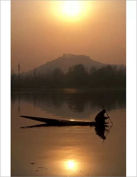 A local fisherman peers into the calm waters of Nigeen Lake on a winter evening in Srinagar