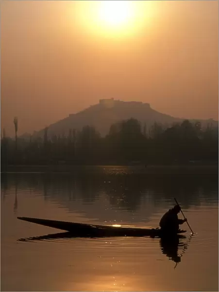 A local fisherman peers into the calm waters of Nigeen Lake on a winter evening in Srinagar