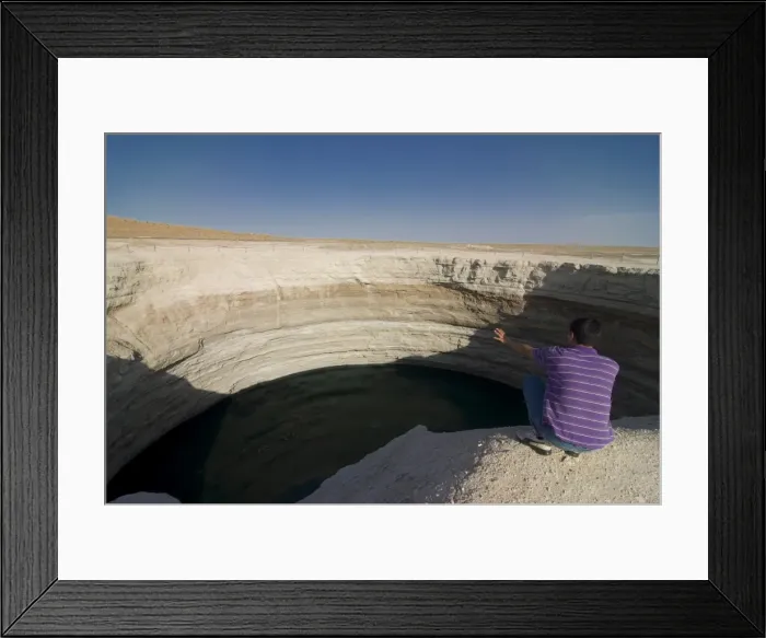 Framed Print : Man sitting on top of a crater filled with water, Karakol desert, Turkmenistan Framed Print : Man sitting on top of a crater filled with water, Karakol desert, Turkmenistan