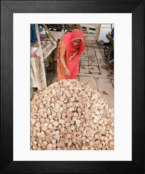 Framed Print : Woman in red sari with pile of terracotta deepak candle dishes for Diwali festival celebrations