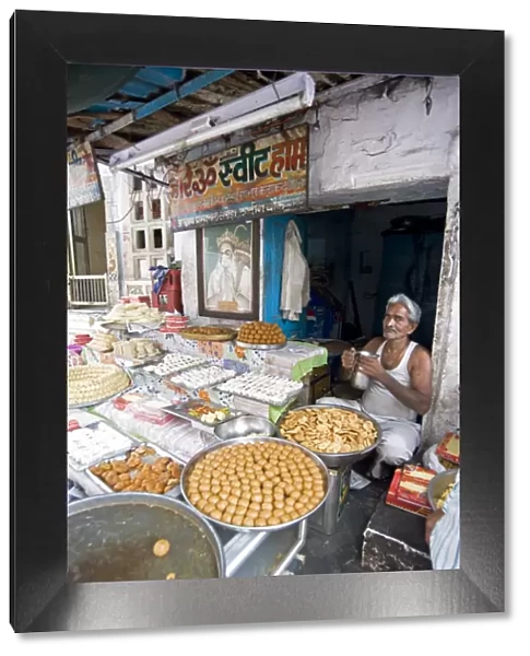 Diwali sweet stall with stallholder and picture of the Hindu god, Hanuman