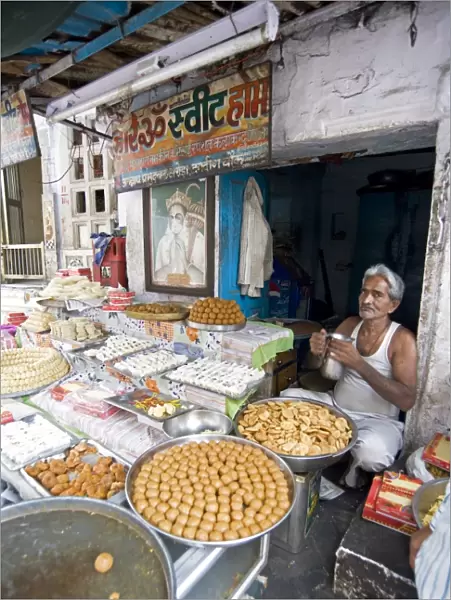 Diwali sweet stall with stallholder and picture of the Hindu god, Hanuman