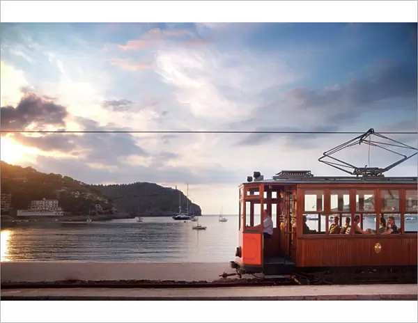 Tram at sunset set against yachts in bay, Soller, Mallorca, Balearic Islands