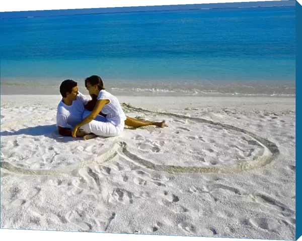 Young couple on beach sitting in a heart shaped imprint on the sand, Maldives