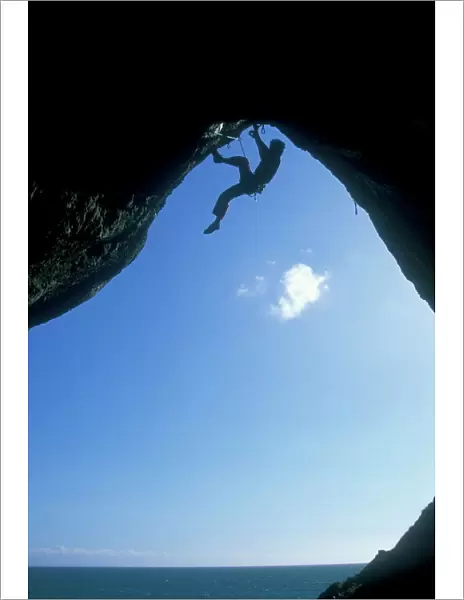 A climber ascending a cave archway at Foxhole, Gower Peninsula, Wales, United Kingdom