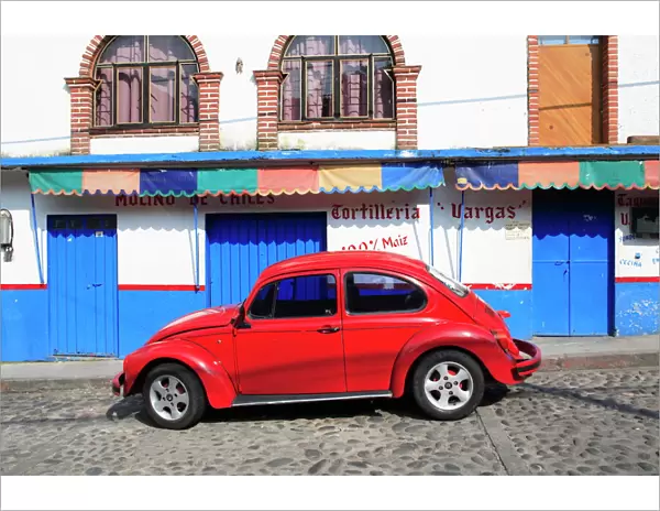 Red Volkswagen Beetle parked on cobblestone street, Tepoztlan, near Mexico City where many city dwellers spend weekends, Morelos, Mexico