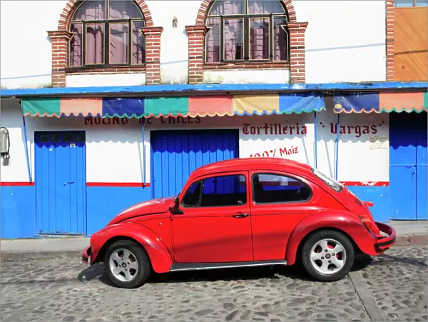 Red Volkswagen Beetle parked on cobblestone street, Tepoztlan, near Mexico City where many city dwellers spend weekends, Morelos, Mexico
