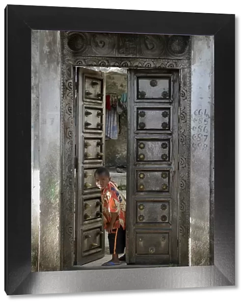 Young little boy looking through a old wooden door, Moroni, Comoros, Africa