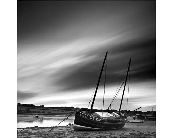 Long exposure used to record moving clouds above old wooden ketch on Aln Estuary at low tide