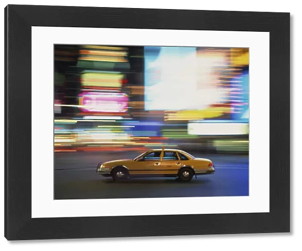 Yellow cab driving past blurred neon lights at night in Times Square in New York