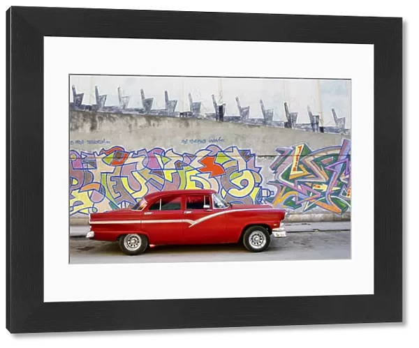 Classic red American car parked in front of grafitti covered wall, Havana