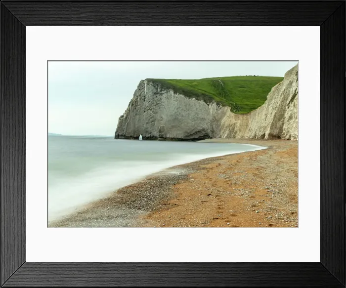 Framed Print : Serene beach with smooth waters, pebbles, and a towering cliff under a cloudy sky at Durdle Door, Jurassic Coast, UNESCO World Heritage Site, Dorset, England, United Kingdom, Europe