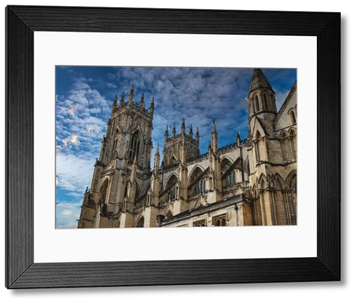 Framed Print : Gothic cathedral tower against a dramatic cloudy sky, showcasing intricate architectural details and spires, ideal for historical or religious themes in York, North Yorkshire, England Framed Print : Gothic cathedral tower against a dramatic cloudy sky, showcasing intricate architectural details and spires, ideal for historical or religious themes in York, North Yorkshire, England