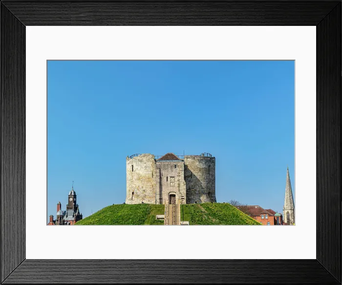 Framed Print : Medieval stone tower on a grassy hill with clear blue sky, flanked by church spires in the background, Clifford's Tower, York, North Yorkshire, England, United Kingdom, Europe